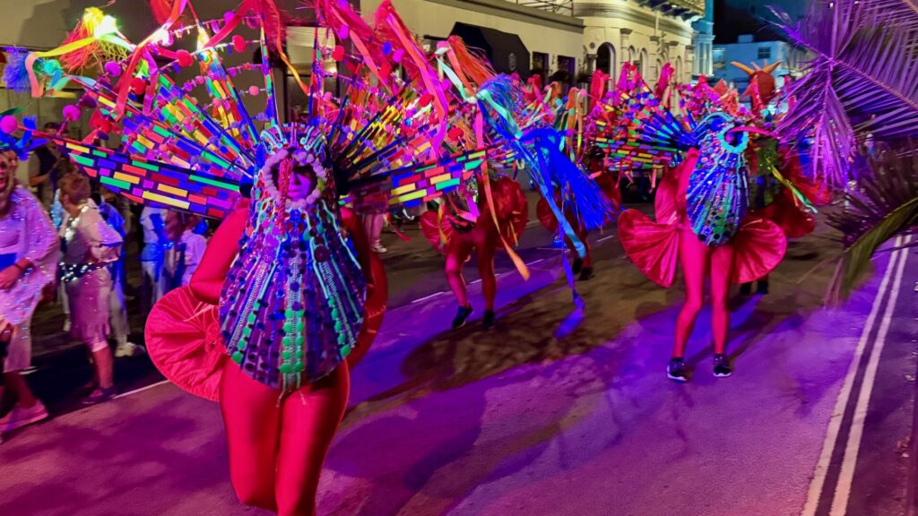 A parade of people dressed in bright colours as human peacocks at Ryde Illuminated Carnival 2024