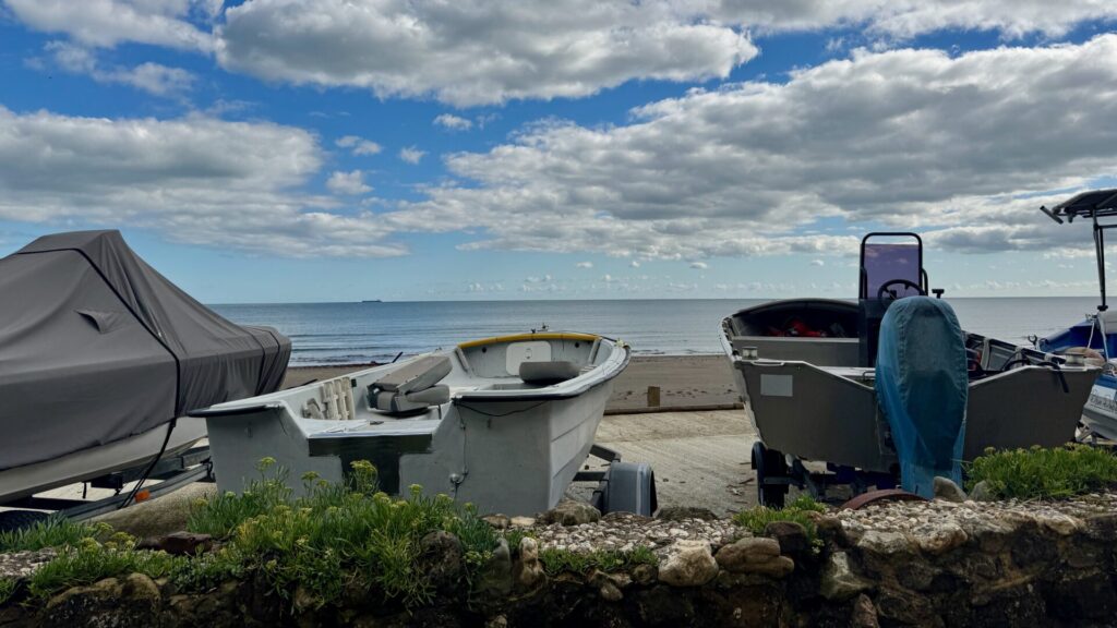 Motor boats on land in the foreground, the sea and blue skies beyond.