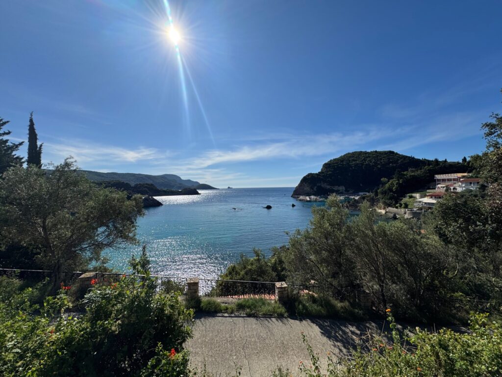 Sunshine over one of the bays at Paleokastritsa, Corfu, with shimmering blue sea and mountains on either side.